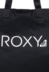 Černá plátěná taška s velkým bílým nápisem "ROXY" a akcentem loga srdce. Vyztužené uši se zkříženým stehem.