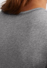 Detaliu al unui tricou din bumbac gri-heather, arătând gulerul rotund și cusăturile vizibile; textură moale cu un finisaj neted, ușor heather.