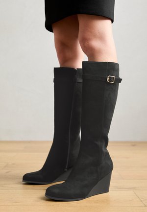 Zwarte suède wedge laarzen met een gladde afwerking, voorzien van een ritssluiting aan de zijkant en een gespaccent op de kuit. Rond toe ontwerp.