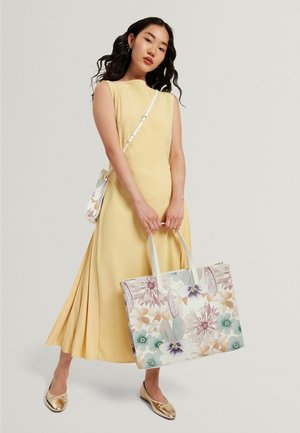 Gele mouwloze jurk met geplooide rok. Bloemenpatroon handtas in pasteltinten met crèmekleurige handvatten, gecombineerd met metalen gouden ballerina's.