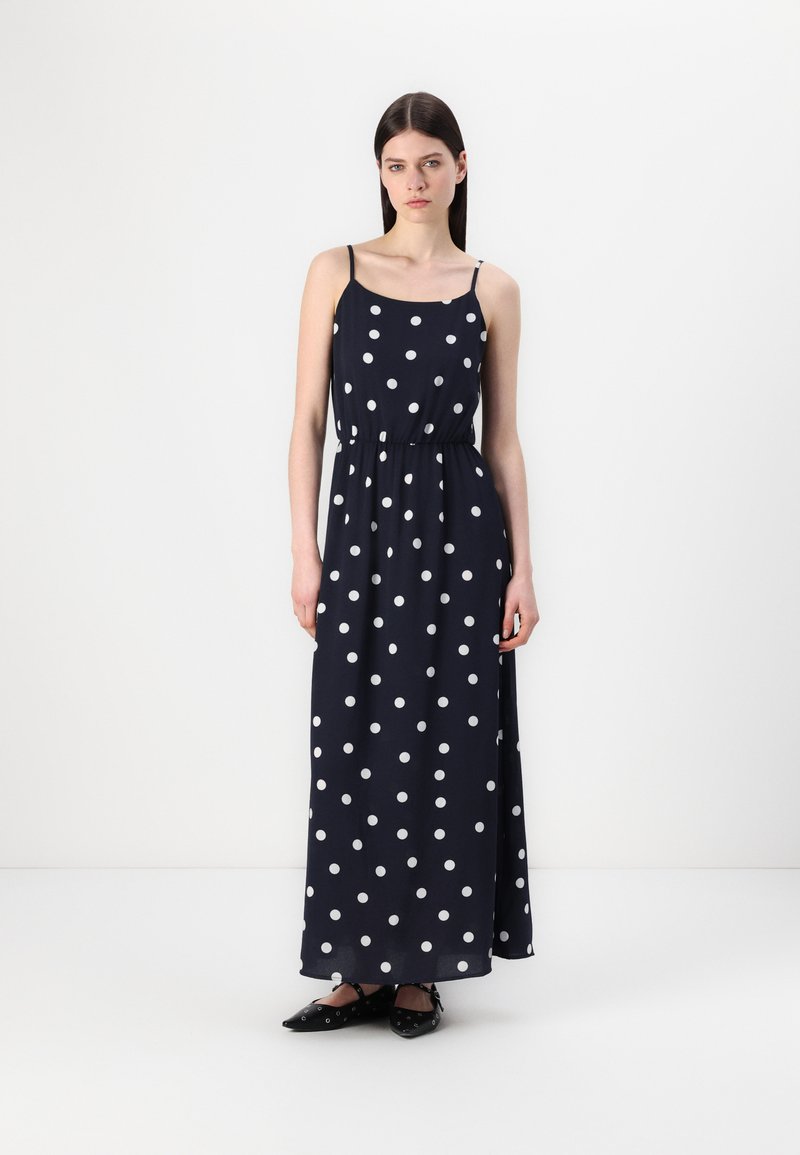 Rochie maxi bleumarin cu buline albe, având bretele subțiri și o talie elastică. Materialul pare ușor, cu o textură netedă.