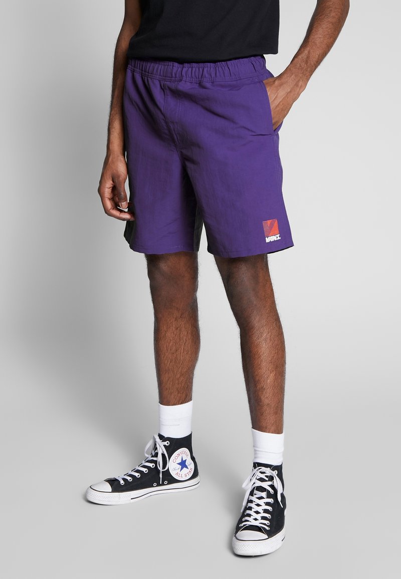 Violetit shortsit, jotka on valmistettu kevyestä kankaasta. Niissä on joustava vyötärönauha, sivutaskut ja kontrastivärinen logoplässi helmassa.