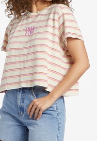 Camiseta corta de manga corta en color crema con rayas horizontales rosas y moradas, que presenta un pequeño logotipo morado en la parte frontal. Ajuste casual, tejido suave.