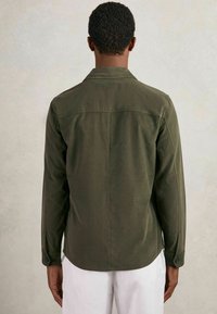 Dunkelgrünes Langarmhemd mit Button-Down-Kragen, abgerundetem Saum und geknöpften Manschetten. Hergestellt aus einem weichen, strukturierten Stoff.