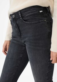 Jeans in denim nero con una vestibilità slim, caratterizzati da un design a cinque tasche, chiusura con bottone e leggero effetto slavato. Abbinati a un maglione color crema.