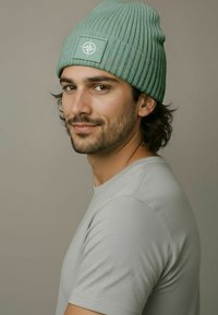 Mint green ribbed beanie with a textured design and a square patch featuring a compass logo, worn with a light gray crew-neck shirt.