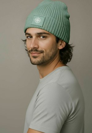 Mint green ribbed beanie with a textured design and a square patch featuring a compass logo, worn with a light gray crew-neck shirt.