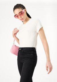 White short-sleeve t-shirt paired with high-waisted black jeans. Model holds a small pink handbag and wears angular pink sunglasses.