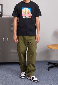 Camisa negra con un gráfico colorido de una tortuga y el texto "SOY RÁPIDO". Combinada con pantalones cargo verdes y zapatillas negras, blancas y rojas.