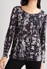 Svart och grå långärmad topp med abstrakt mönster, rund halsringning och rynkad detalj vid bröstet; mjukt, lätt material.