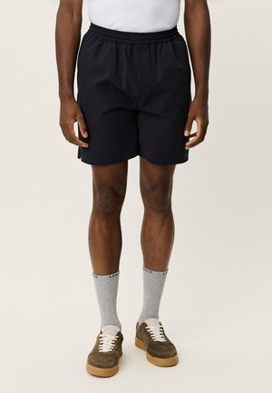 Sorte atletikshorts lavet af letvægtsmateriale med elastisk taljebånd. Bæres med grå sokker og brune sneakers.