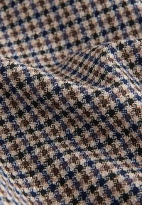 Textile in a checkered pattern featuring beige, brown, navy, and black colors with a textured finish. Soft and draped appearance.