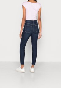 Jeans skinny de mezclilla oscura con una cintura alta, que cuentan con dos bolsillos traseros y costuras en contraste, combinados con una camisa ajustada de color rosa claro.