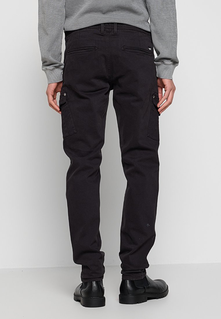 Zwarte cargobroek met een getailleerd ontwerp, voorzien van meerdere zijzakken en een gladde textuur. Gecombineerd met zwarte schoeisel.