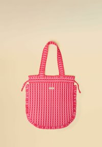 Rožinės ir raudonos spalvos languotas nešiojimo krepšys su raukšlėtomis kraštinėmis ir dviem rankenomis, gulintis ant beige fono.