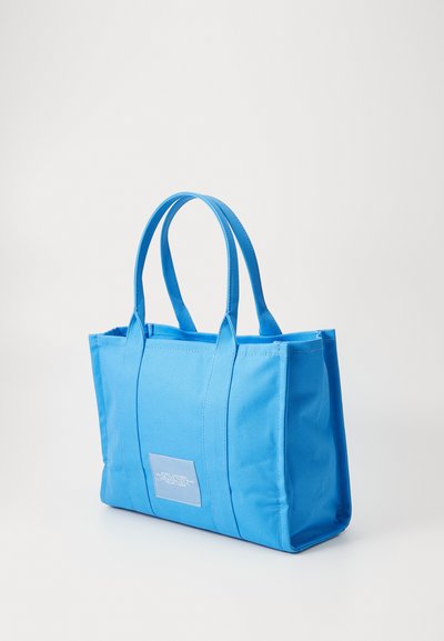 Borsa a spalla in tessuto blu con due manici superiori, forma rettangolare e una patch etichetta sul fronte. Superficie strutturata con cuciture rinforzate.