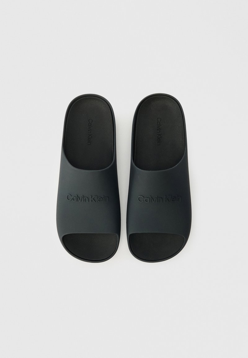 Schwarze Gummisandalen mit offenen Zehen, ausgestattet mit einem geprägten "Calvin Klein"-Logo auf dem Obermaterial und einer glatten, matten Textur.