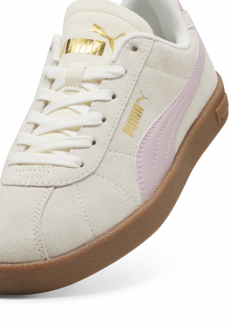 Baskets en suede blanc avec des accents rose clair, logo doré sur la languette et semelle en caoutchouc texturé brun. Design minimaliste avec des lignes épurées.