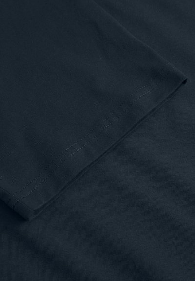 Mørk navy bomulds t-shirt med en glat tekstur, der har en foldet kant og pænt syede kanter, hvilket fremhæver enkelhed i designet.