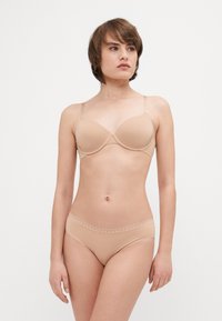 Beige underwire-bh med glatte kopper og justerbare stropper, kombinert med matchende bikini-truser med bølgede kanter i midjen.
