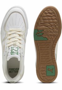 Baskets en cuir blanc avec des accents crème, un design perforé à l'avant, un logo vert sur le côté, et une semelle extérieure en caoutchouc avec des crampons texturés.