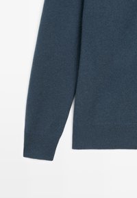 Pletený svetr v tmavě modré barvě, s jemnou texturou, běžným střihem, dlouhými rukávy a žebrovaným lemem a manžetami.