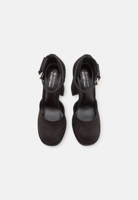 Escarpins noirs en suède vegan avec bout fermé, bride de cheville et talon épais. Texture lisse avec un design minimaliste.