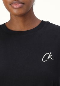 Svart bomull t-skjorte med rund hals, med en hvit brodert "CK" logo på venstre bryst. Glatt tekstur, uformell design.