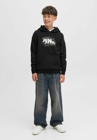 Felpa nera con design grafico in bianco, tasca frontale e cappuccio con cordino. Abbinata a jeans in denim larghi e sbiaditi e sneakers bianche.