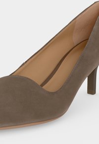 Chaussure à talons hauts en daim marron avec bout arrondi et talon effilé, vue en gros plan de profil sur fond blanc.