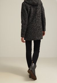 Czarny i szary wzorzysty wełniany płaszcz z kapturem, sięgający do połowy uda, w połączeniu z czarnymi dopasowanymi dżinsami i botkami za kostkę z grubą podeszwą.