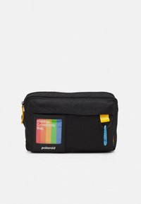 Borsa a tracolla nera in ripstop con tasca frontale con cerniera e dettagli gialli. Presenta un'etichetta multicolore e un tiralampo blu.