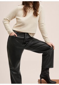 Suéter crema y pantalones de imitación cuero negros de cintura alta. Textura elegante con un ajuste relajado, combinados con botas negras de tacón alto hasta la rodilla.