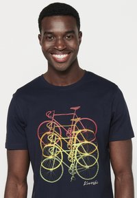 Camiseta de color azul marino hecha de algodón con un estampado gráfico de bicicletas superpuestas en tonos rojos, naranjas y amarillos. Presenta un escote redondo.