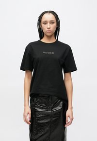 Černé bavlněné tričko s krátkými rukávy a kulatým výstřihem s logem "PINKO" ve zlaté barvě. Doplněno o lesklou černou plisovanou sukni.