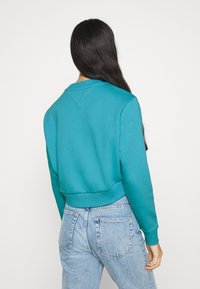 Turkost sweatshirt med avslappnad passform, ribbade muddar och midja. Slät yta och rundad halsringning, i kombination med ljusblå jeans.