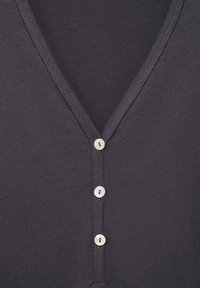 Tessuto grigio scuro con un design a V e quattro bottoni bianchi sul davanti, con cuciture visibili lungo i bordi. Texture liscia.