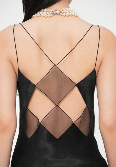 Czarna sukienka z przezroczystym tyłem z siateczki z diamentowymi wycięciami, cienkimi ramiączkami i fakturowanym wykończeniem. Perłowy naszyjnik podkreśla linię dekoltu.