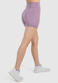 Pantaloni corti viola a vita alta con una texture liscia e materiale elasticizzato. Indossati con sneakers bianche dotate di un design in mesh.