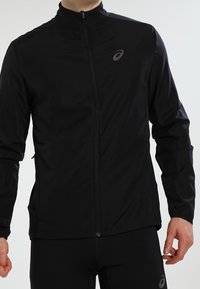 Schwarze Sportjacke mit Stehkragen, durchgehendem Reißverschluss und dezentem Logo auf der Brust. Glatte Textur, taillierte Passform und lange Ärmel.