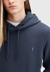 Navy blue hooded sweatshirt with a black horned skull logo, featuring a drawstring hood and soft fabric texture.