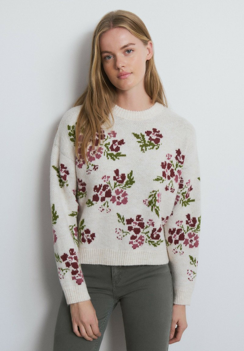 Suéter de punto en color crema con patrones florales en rojo oscuro y verde. Cuello redondo, mangas largas, dobladillo acanalado y tela texturizada.