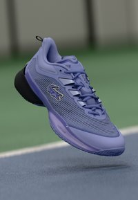 Botte de sport violette avec tige en mesh, semelle noire et accents réfléchissants ; possède des lacets et un logo bien visible sur le côté.
