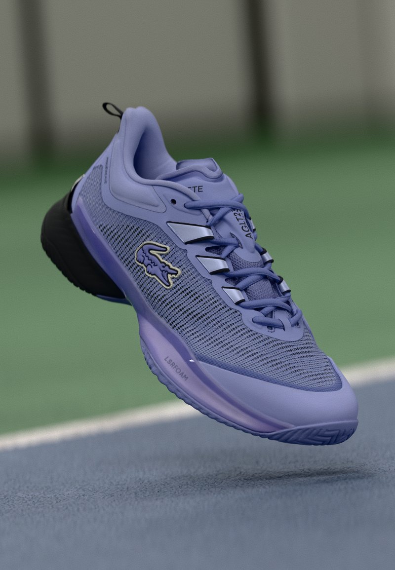 Botte de sport violette avec tige en mesh, semelle noire et accents réfléchissants ; possède des lacets et un logo bien visible sur le côté.