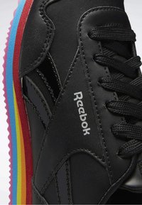 Baskets noires Reebok avec lacets noirs et une semelle rayée arc-en-ciel comprenant des couches bleues, rouges, jaunes, orange et roses.