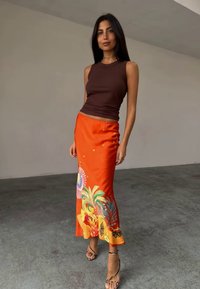 Bruine mouwloze top met een aansluitend ontwerp, gecombineerd met een levendige oranje satijnen rok met bloemmotieven en accenten aan de zoom.