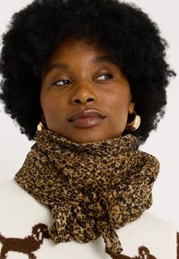 Bufanda de estampado de leopardo en marrón y negro, fabricada en un material ligero con una textura suave, anudada al cuello y con un diseño suelto y fluido.