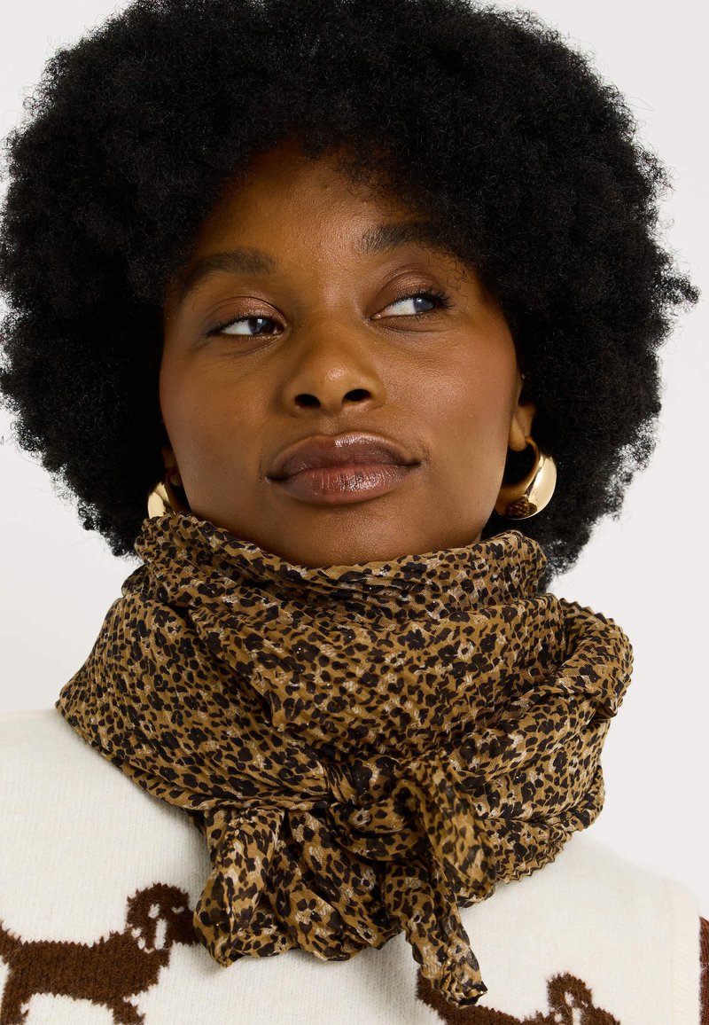 Bufanda de estampado de leopardo en marrón y negro, fabricada en un material ligero con una textura suave, anudada al cuello y con un diseño suelto y fluido.