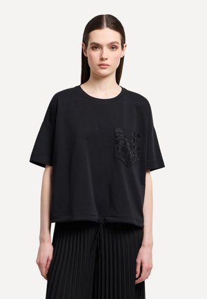 Maglietta nera oversize con maniche corte, scollatura rotonda e tasca testurizzata con un design geometrico. Tessuto morbido, vestibilità comoda.