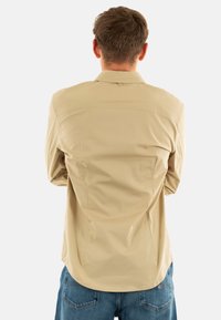 Camicia beige con bottoni, colletto, vestibilità su misura, cuciture sulle spalle e un tessuto leggero e morbido, abbinata a jeans in denim blu.